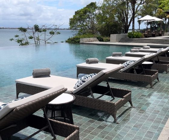 Row of woven sun loungers in the pool shallows